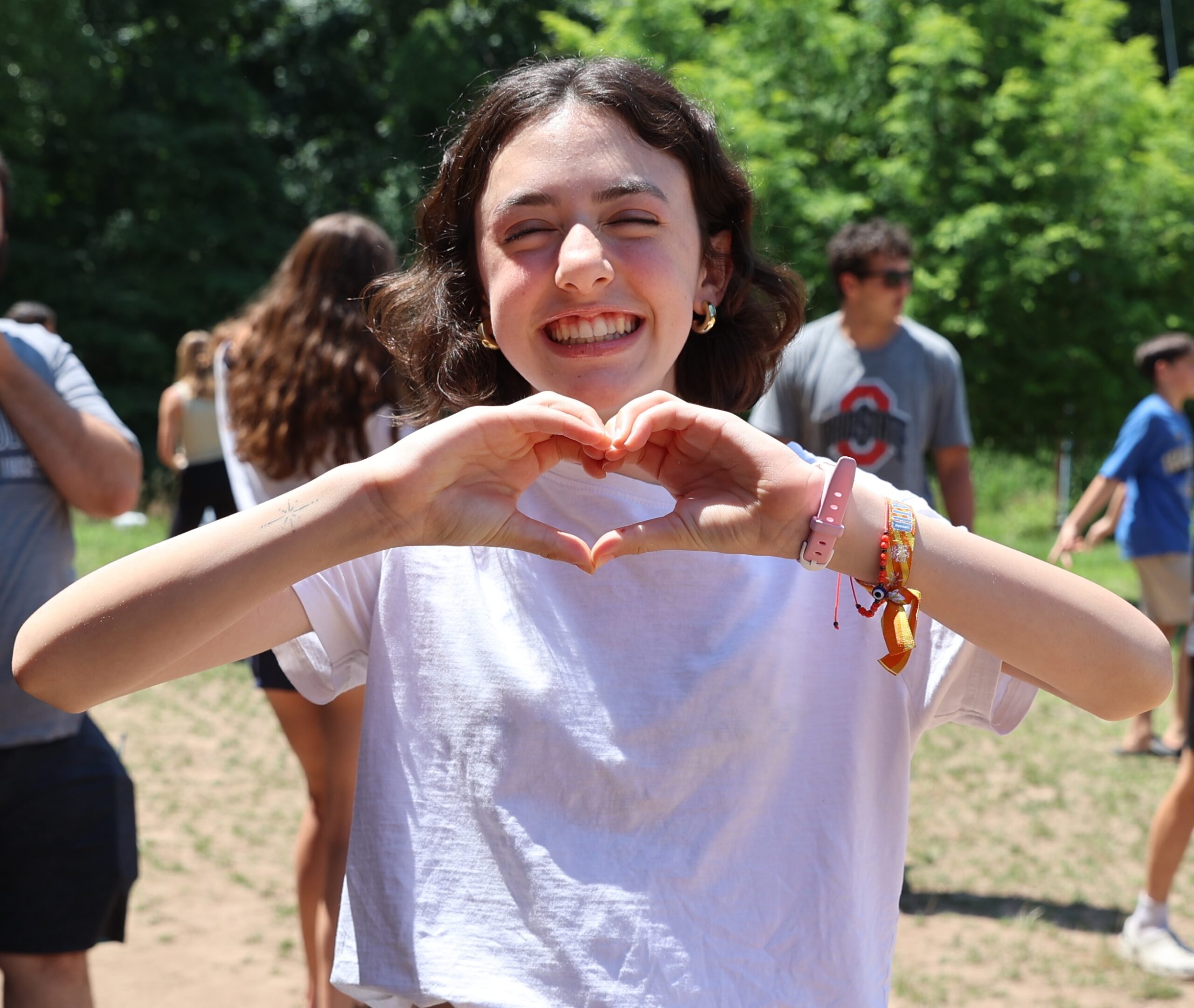 Teen making a heart shape with her hands, smiling outdoors